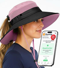Woman in light pink and black GearTOP ponytail hat checks UV levels with SunUp app, emphasizing sun safety for travel.