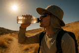 Extreme heat sun protection: hiker in UPF 50+ wide-brim hat drinking water on a scorched trail at midday