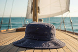 Wide-brim UPF sailing hat on a sailboat deck with blue ocean and white sails in background