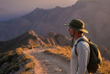 Man wearing a UPF 50+ wide-brim sun hat on a sunny hiking trail at golden hour