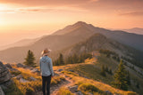 Hiker on sunny mountain trail wearing UPF sun hoodie and wide-brim sun hat during golden hour