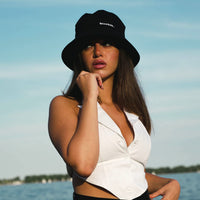 Woman wearing the black Reset Bucket Hat with a timeless bucket hat silhouette, offering breathable comfort and stylish sun protection for travel, beach days, and everyday wear.